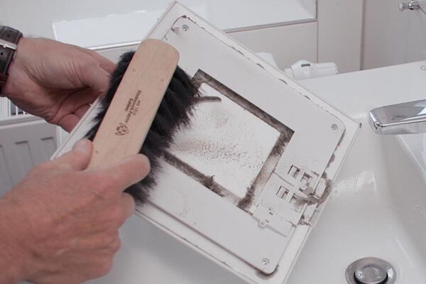 Nahaufnahme eines Luftfilters, der gereinigt wird. Symbolbild für Wartung und Sauberkeit in Wohngebäuden.