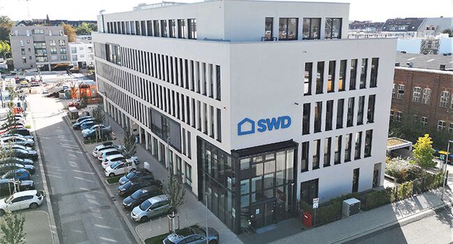 Verwaltungsgebäude der SWD mit großflächigen Fenstern und einem klaren, weißen Design. Der Eingangsbereich ist gut sichtbar, umgeben von einem Parkplatz.
