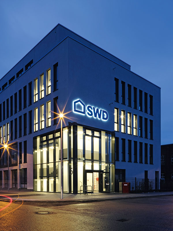 Ein Foto des beleuchteten Hauptgebäudes der Stadtwerke Düsseldorf bei Nacht, das die moderne Architektur und Unternehmenspräsenz in der Stadt hervorhebt.