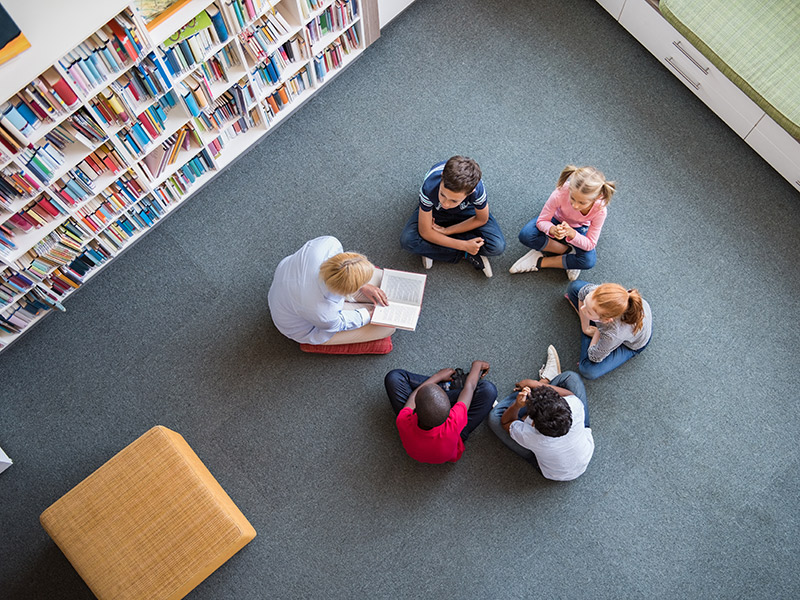 Ein Bild von Kindern verschiedener Herkunft, die zusammen in einer Bibliothek sitzen und lesen, was die Bedeutung von Bildung und Inklusion betont.