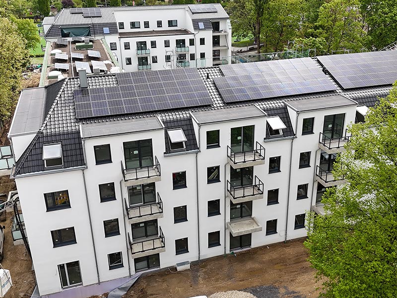 Luftaufnahme eines Neubaus mit Solarpanelen auf dem Dach. Die Gebäudeplanung vereint moderne Architektur mit umweltfreundlicher Energie.